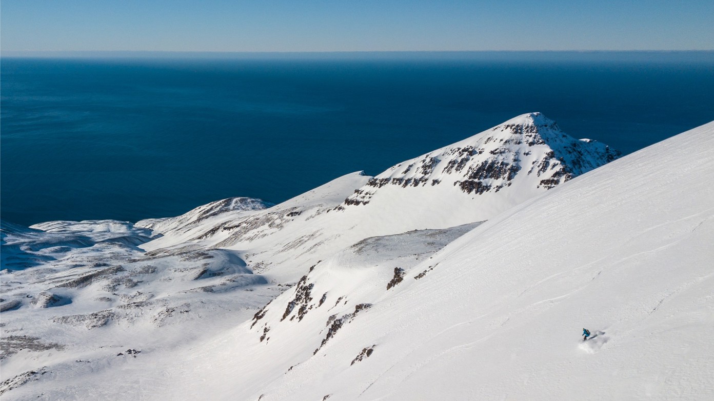 An aerial of a lone person skiing down a steep snow-covered mountain.